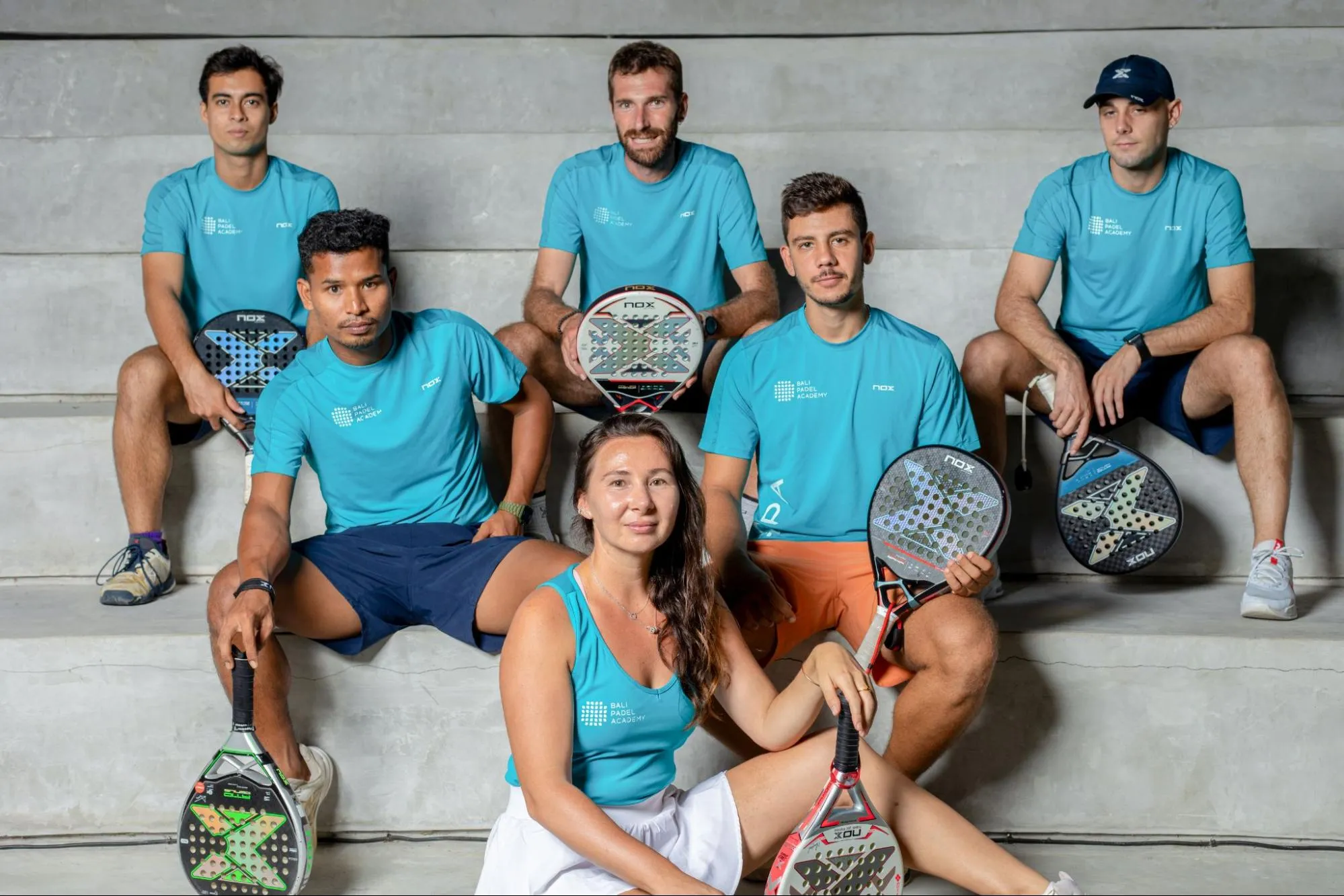 Coaches from Bali Padel Academy posed on concrete steps in matching teal shirts, holding padel rackets