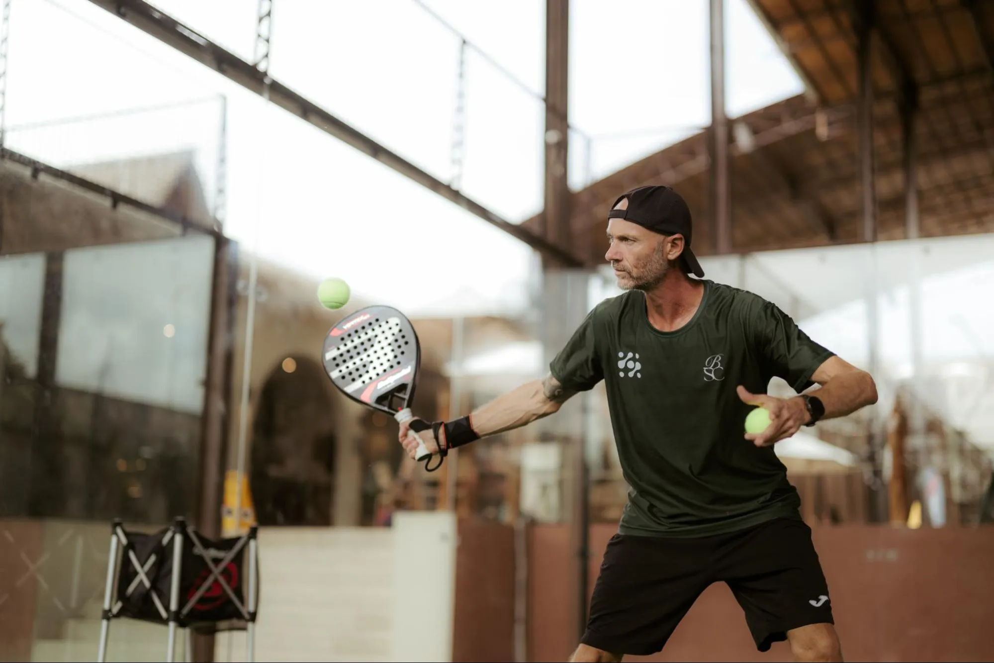 Davide Tortora playing padel, racket back to strike, wearing a Bali Social Club shirt