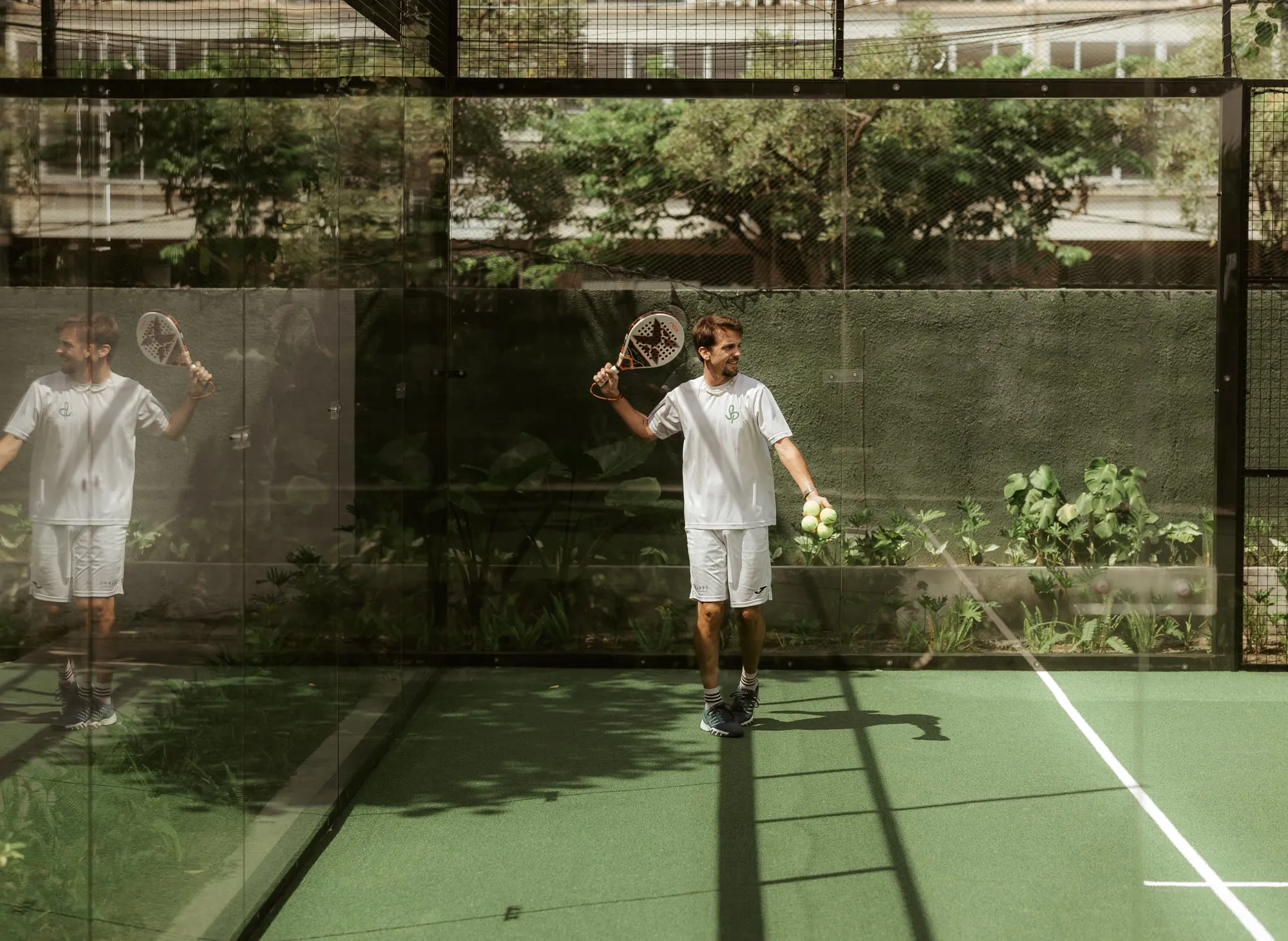 Padel coach standing on court with a racket and balls