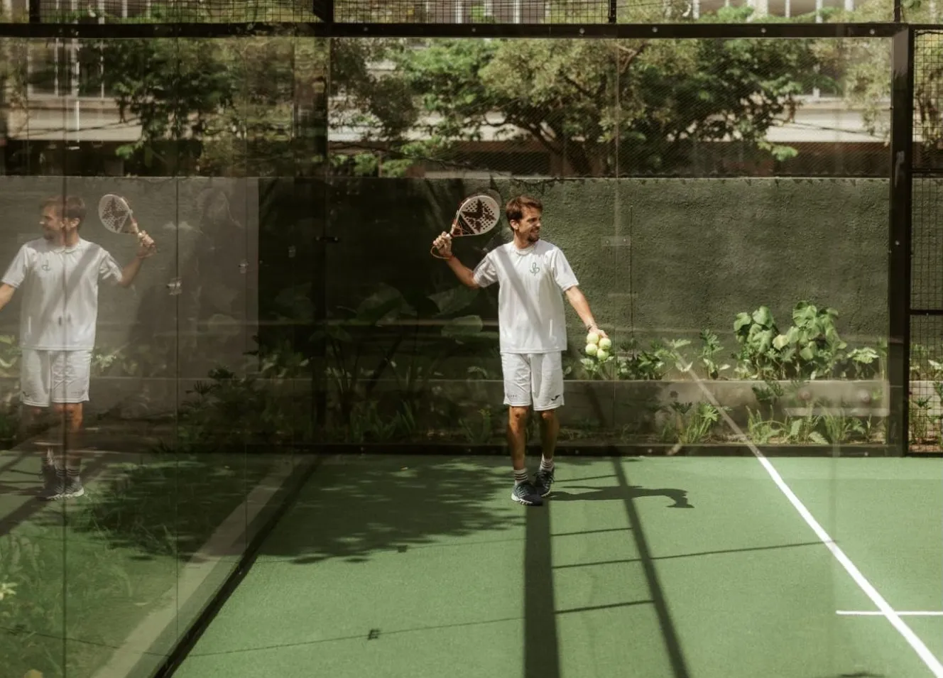 Kilian Manzano on a padel court holding a racket and balls, tropical trees visible through the glass