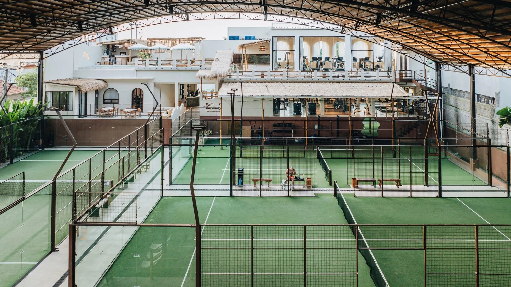 Covered padel courts beside a clubhouse with gym and terrace